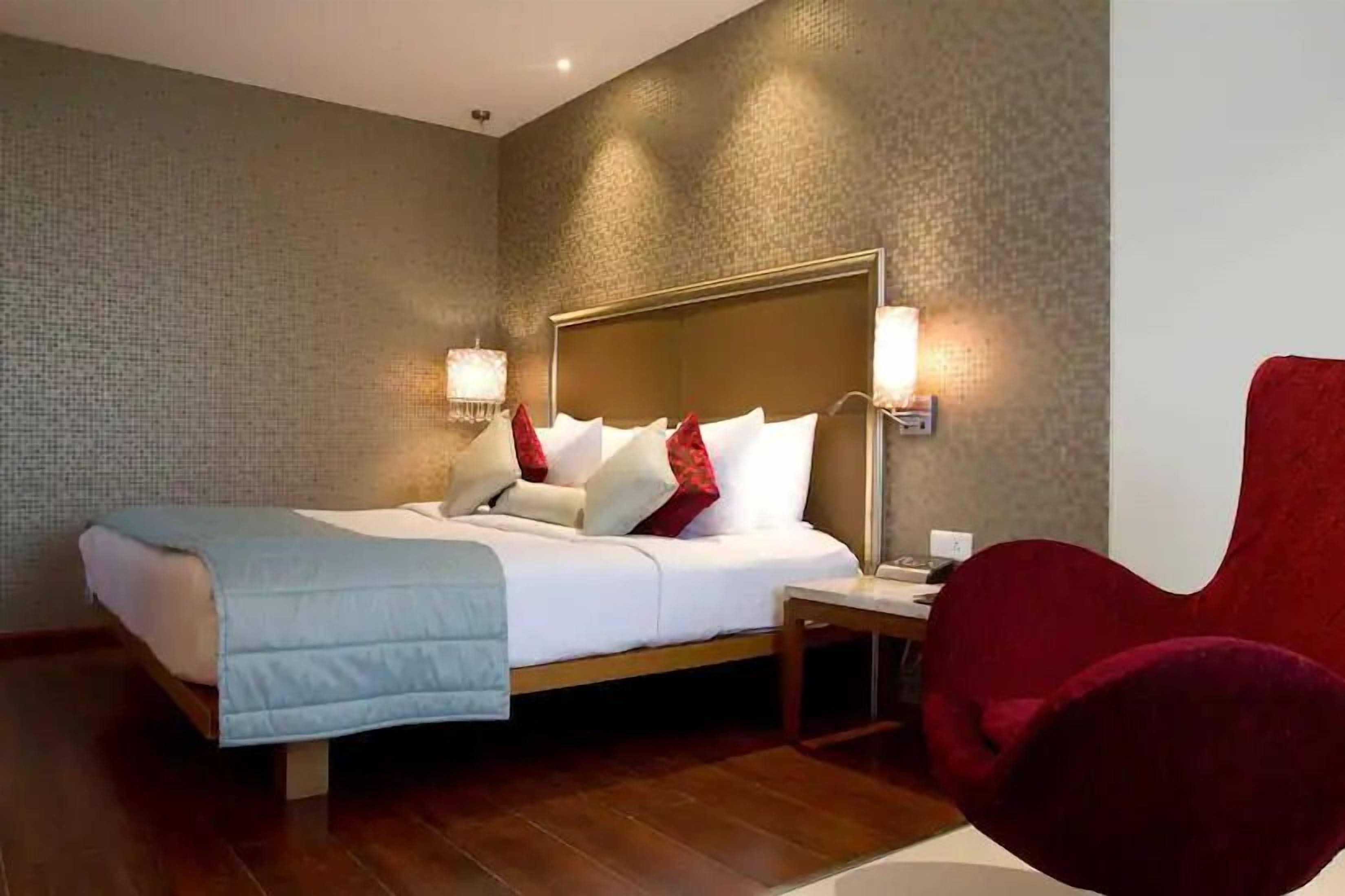 Una habitación de hotel con una cama, mesitas de noche, una silla roja y una pared con textura.