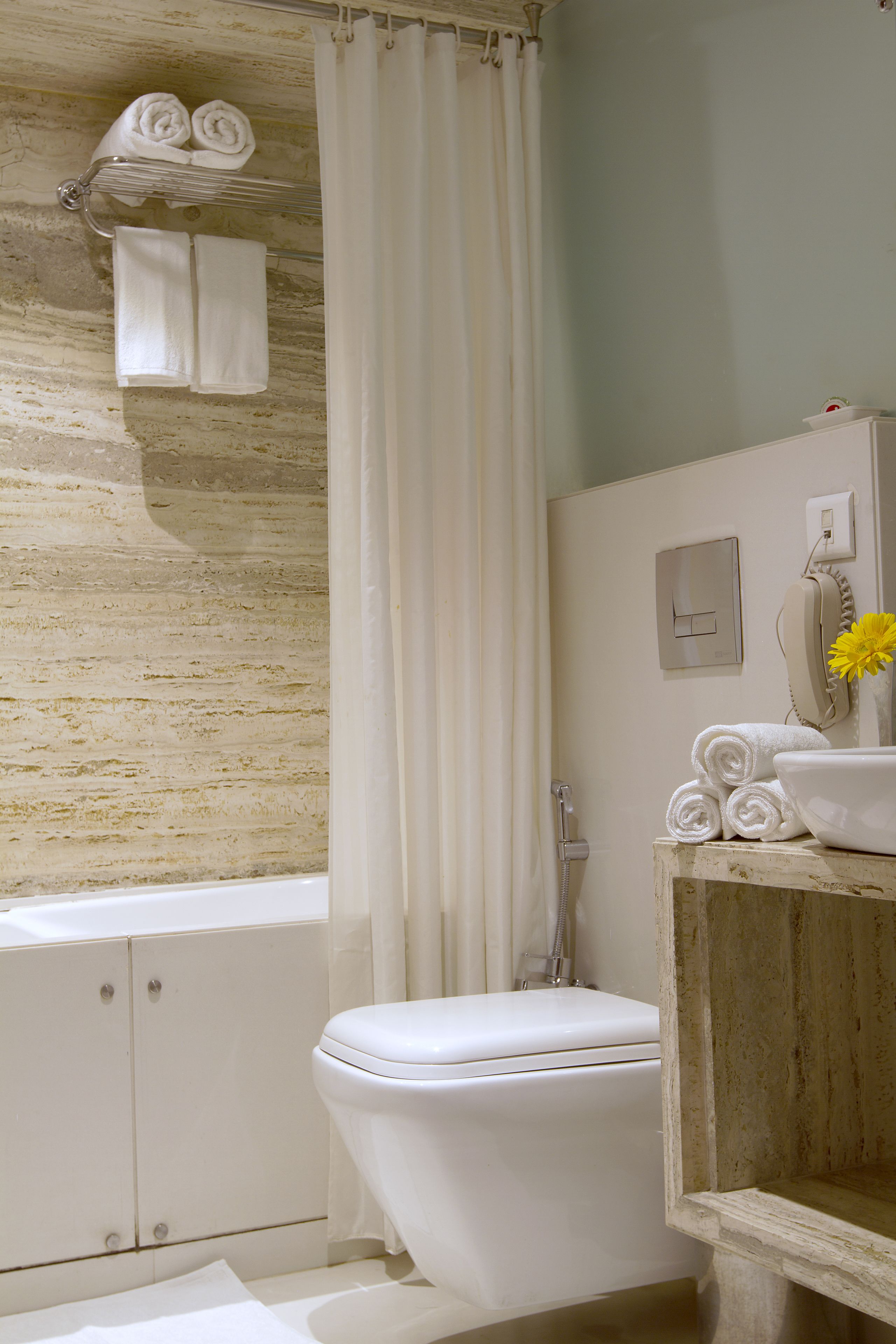 A bathroom with a bathtub, toilet, and a shower curtain. There are towels on a rack and a flower vase on the counter.