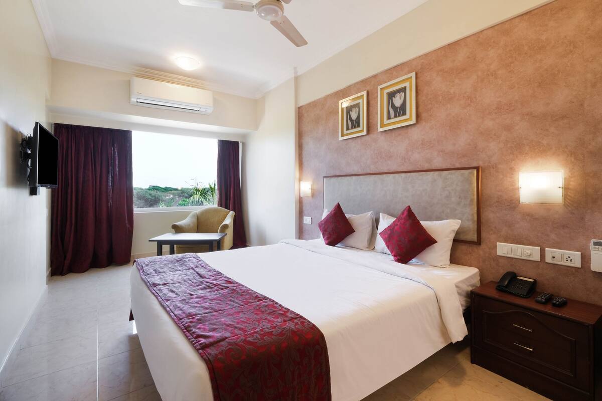 A hotel room with a large bed, a desk, a chair, a TV, and a window with curtains.