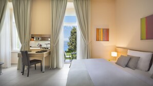 Quarto de hotel com cama, escrivaninha, cadeira e vista para uma árvore pela janela.