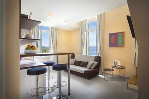 Una sala moderna con un sofá, taburetes de bar, una mesa de comedor y vista al mar.