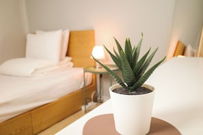 A neatly made bed with white linens, a small potted plant on a bedside table, and a bedside lamp. - Starria Hostel Foreign Guest Only (Seoul)