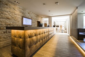 A reception area with a stone wall, a wooden reception desk, and a view into the hotel lobby. - RiKu HOTEL Neu-Ulm (Neu-Ulm)