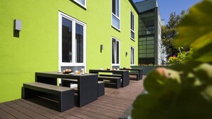An outdoor patio with wooden flooring and black wicker furniture. - RiKu HOTEL Neu-Ulm (Neu-Ulm)