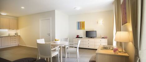 Una sala de estar moderna con un sofá, una mesa de comedor con sillas, un televisor y un escritorio pequeño con una lámpara.