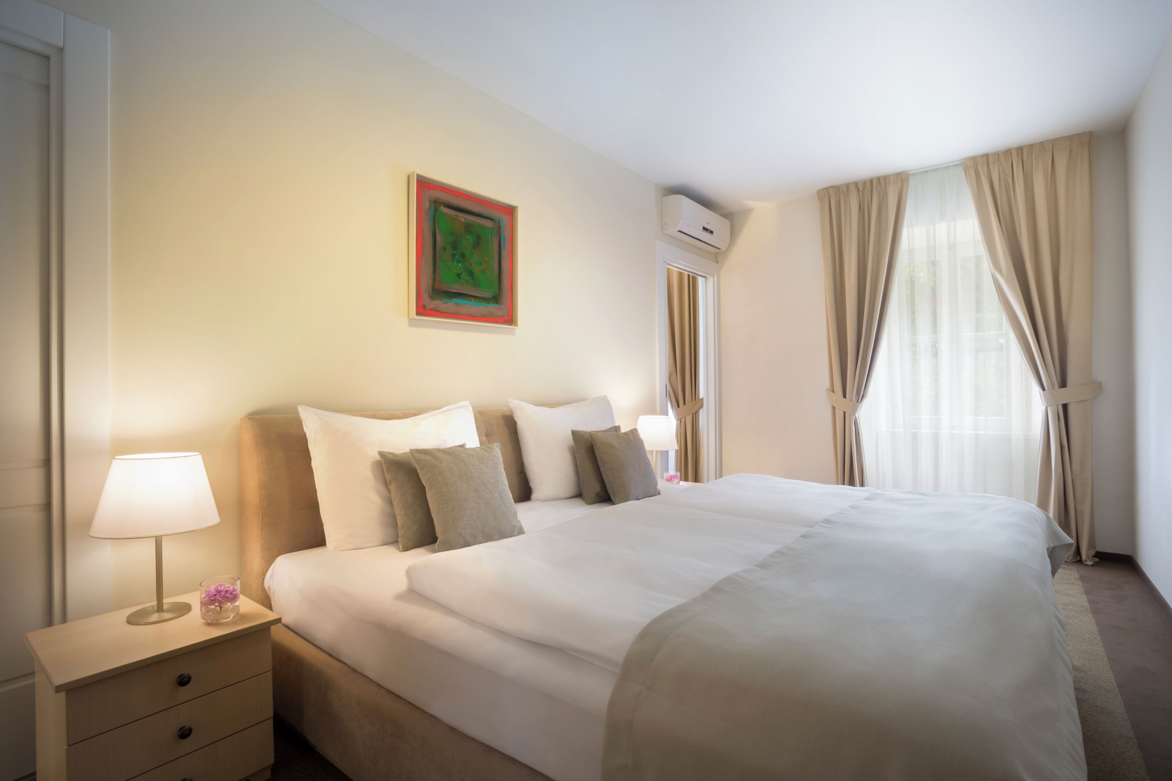 A hotel room with a bed, bedside tables, a lamp, and a window with curtains.