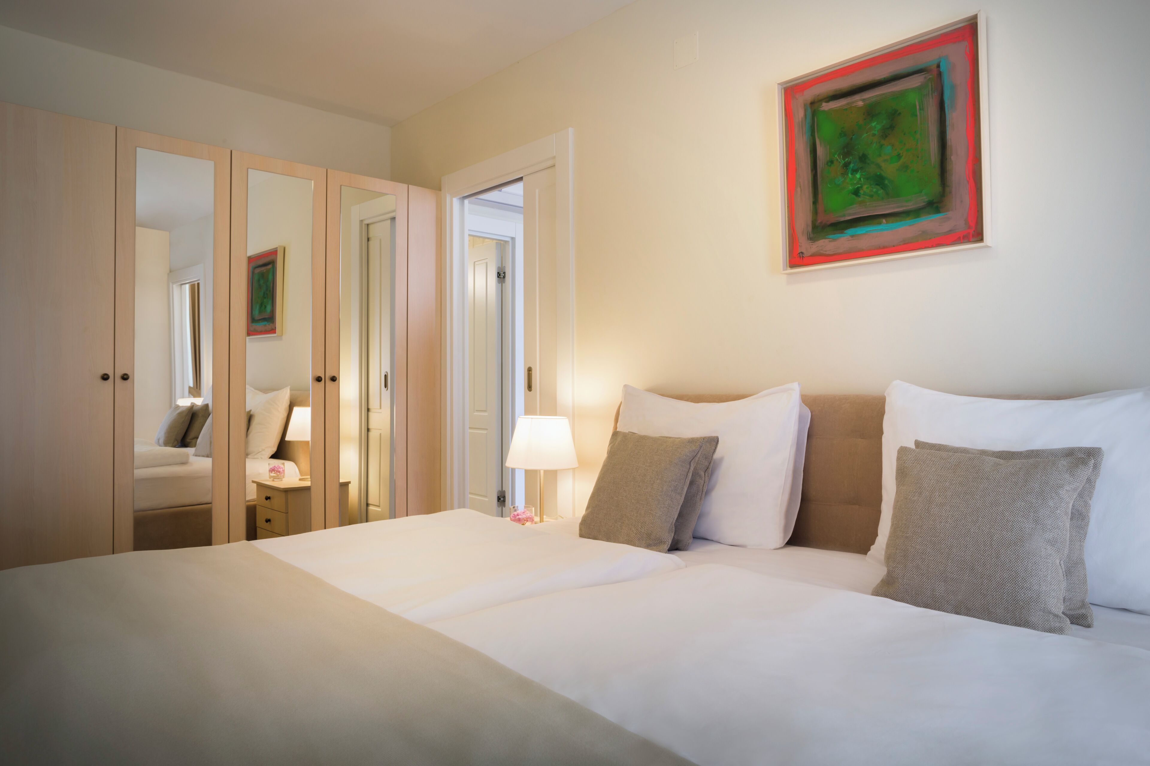 A hotel room with a large bed, a bedside table, a lamp, and a painting on the wall.