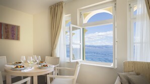 A dining area with a table set for two, a sofa, and a view of the sea through large windows. - Apartments Belvedere - Liburnia (Lovran)