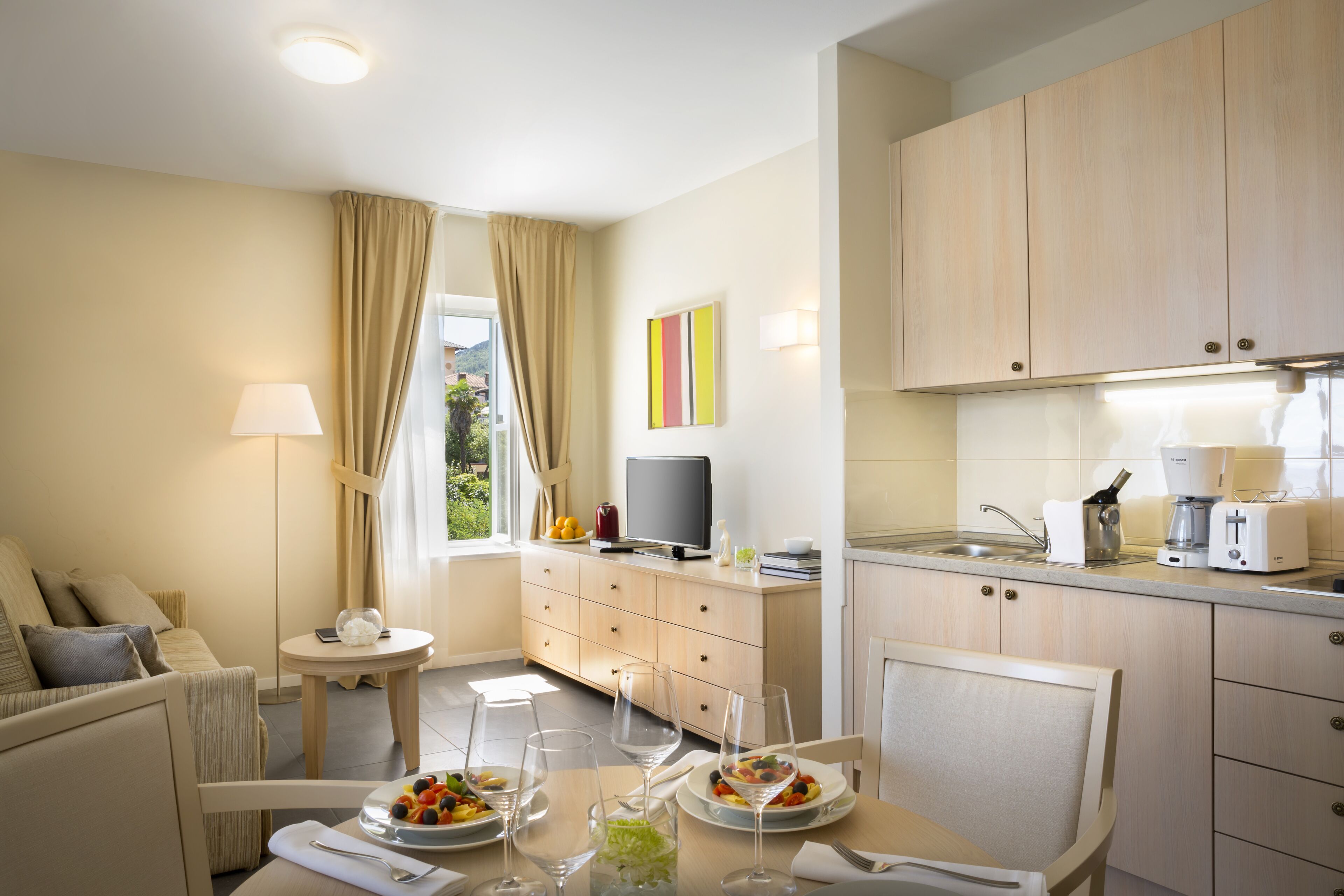 A modern hotel room with a dining area, kitchenette, and a sofa.