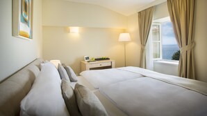 A hotel room with two beds, a bedside table with a lamp, a window with curtains, and a painting on the wall. - Apartments Belvedere - Liburnia (Lovran)