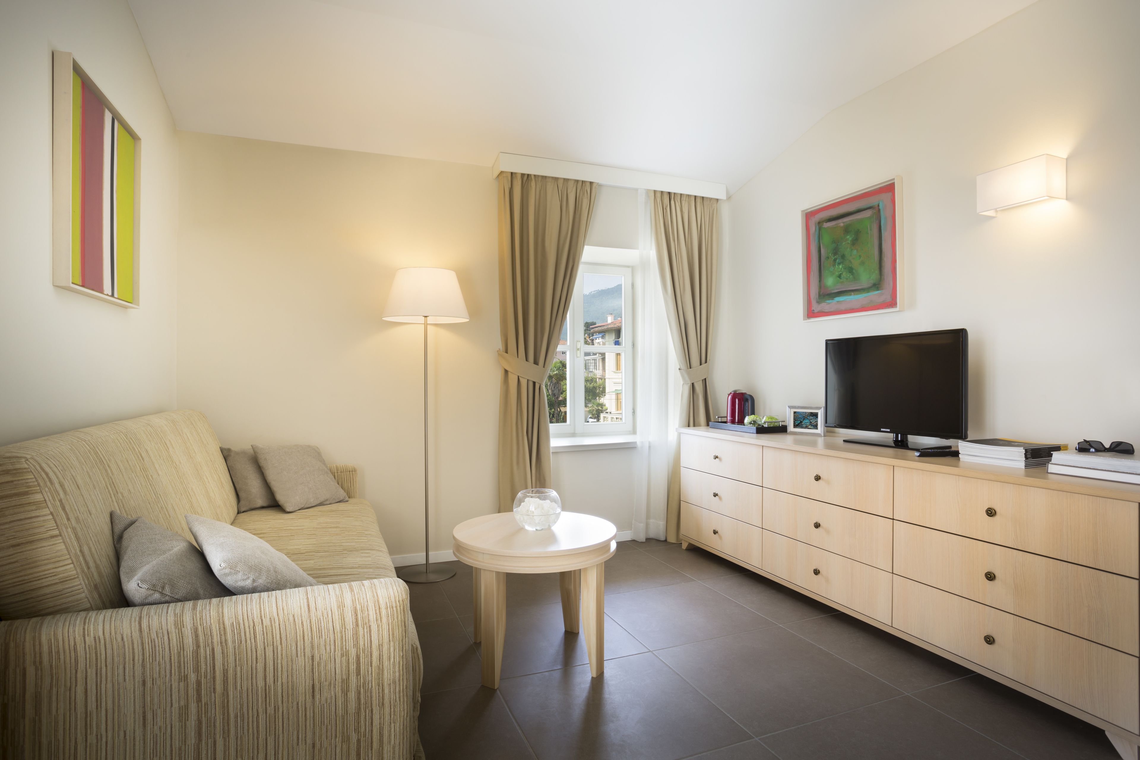 A modern hotel room with a sofa, a small round table, a TV, and a cabinet.