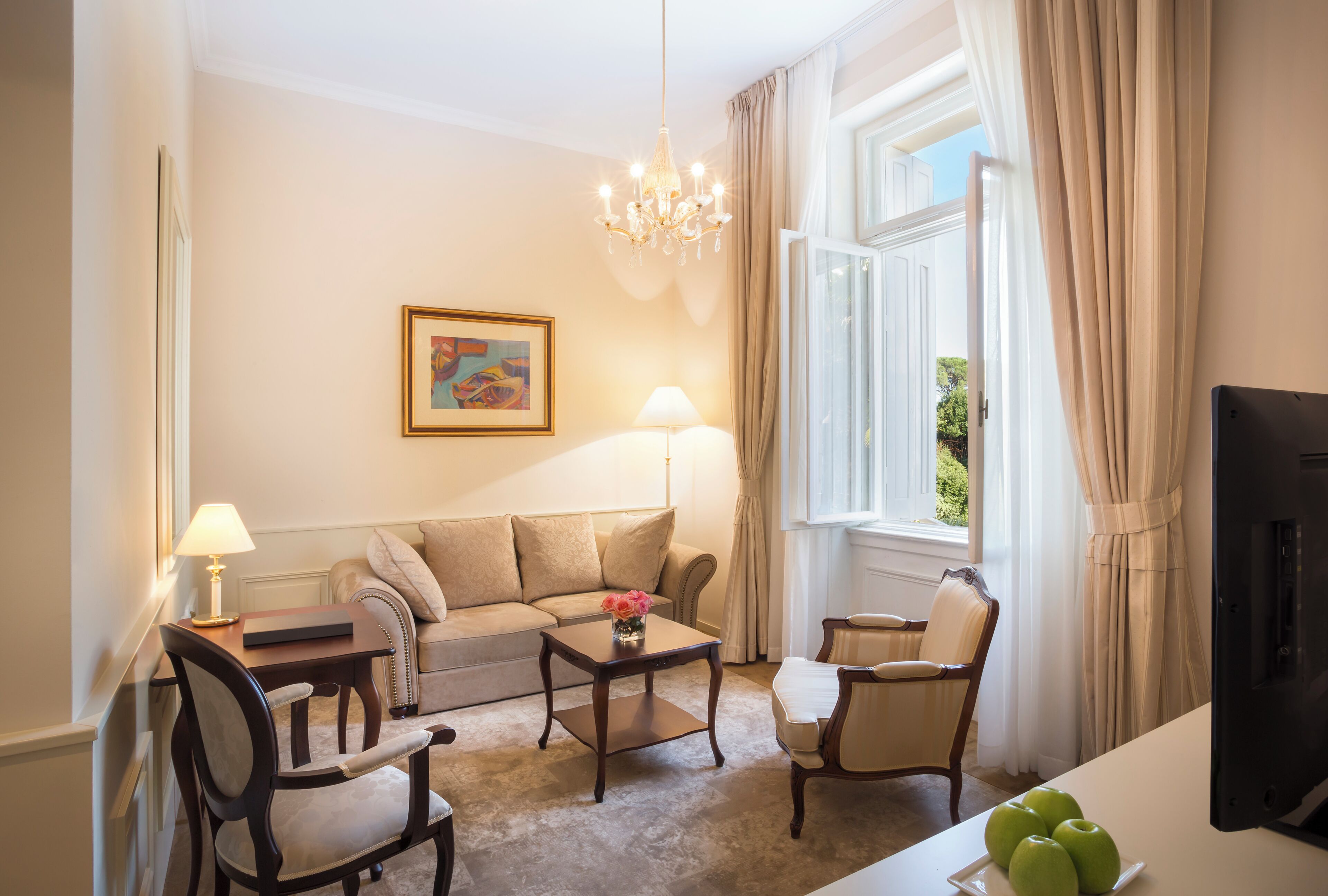A living room with a sofa, armchairs, a coffee table, a TV, and a window with curtains.