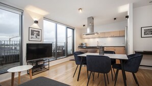 A modern apartment with a living room, dining area, and kitchen. It features large windows, a flat-screen TV, a dining table with chairs, and a kitchen with cabinets and a stove. - Planet Apartments (Reykjavik)