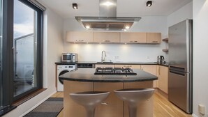 A modern kitchen with a central island, stainless steel appliances, and a large window. - Planet Apartments (Reykjavik)