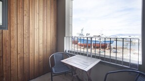 A balcony with wooden paneling, a table, two chairs, and a view of boats and a ship docked at a marina. - Planet Apartments (Reykjavik)