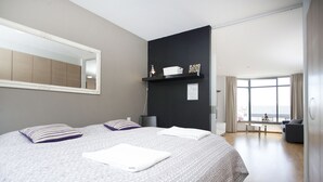 A modern hotel room with a large bed, a mirror, a black shelf with toiletries, and a view of the city through large windows. - Planet Apartments (Reykjavik)