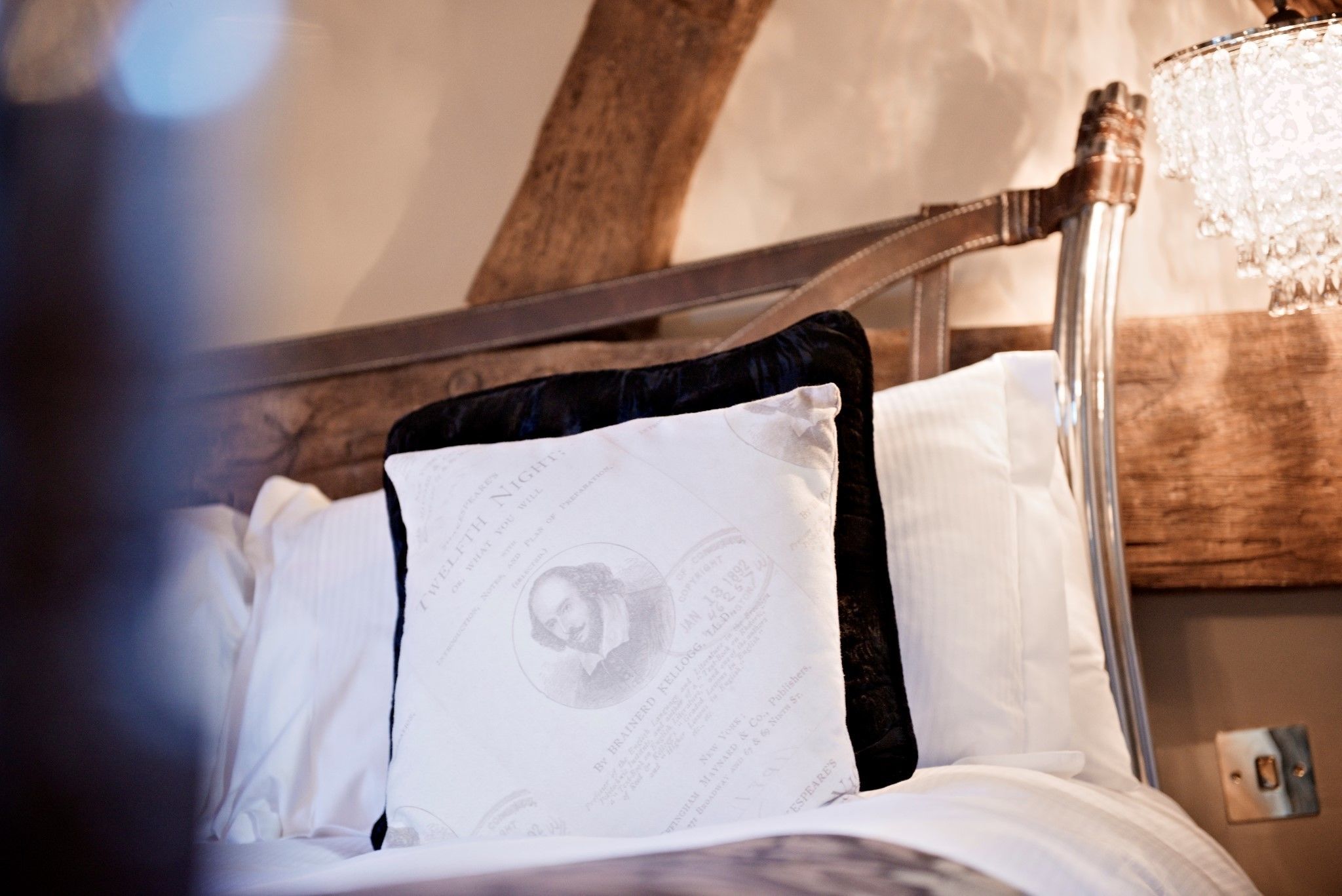 A bed with a wooden headboard, white bedding, and a decorative pillow with text.