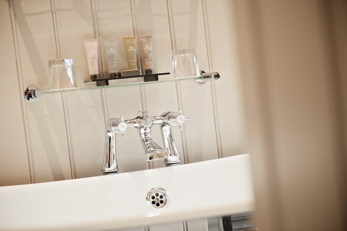 A bathroom with a white sink, chrome faucet, and a glass shelf above it.