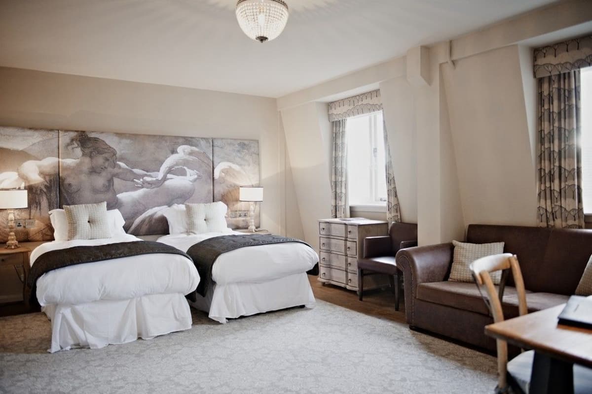 Une chambre d’hôtel avec deux lits, un canapé, une petite table et un grand tableau au mur.