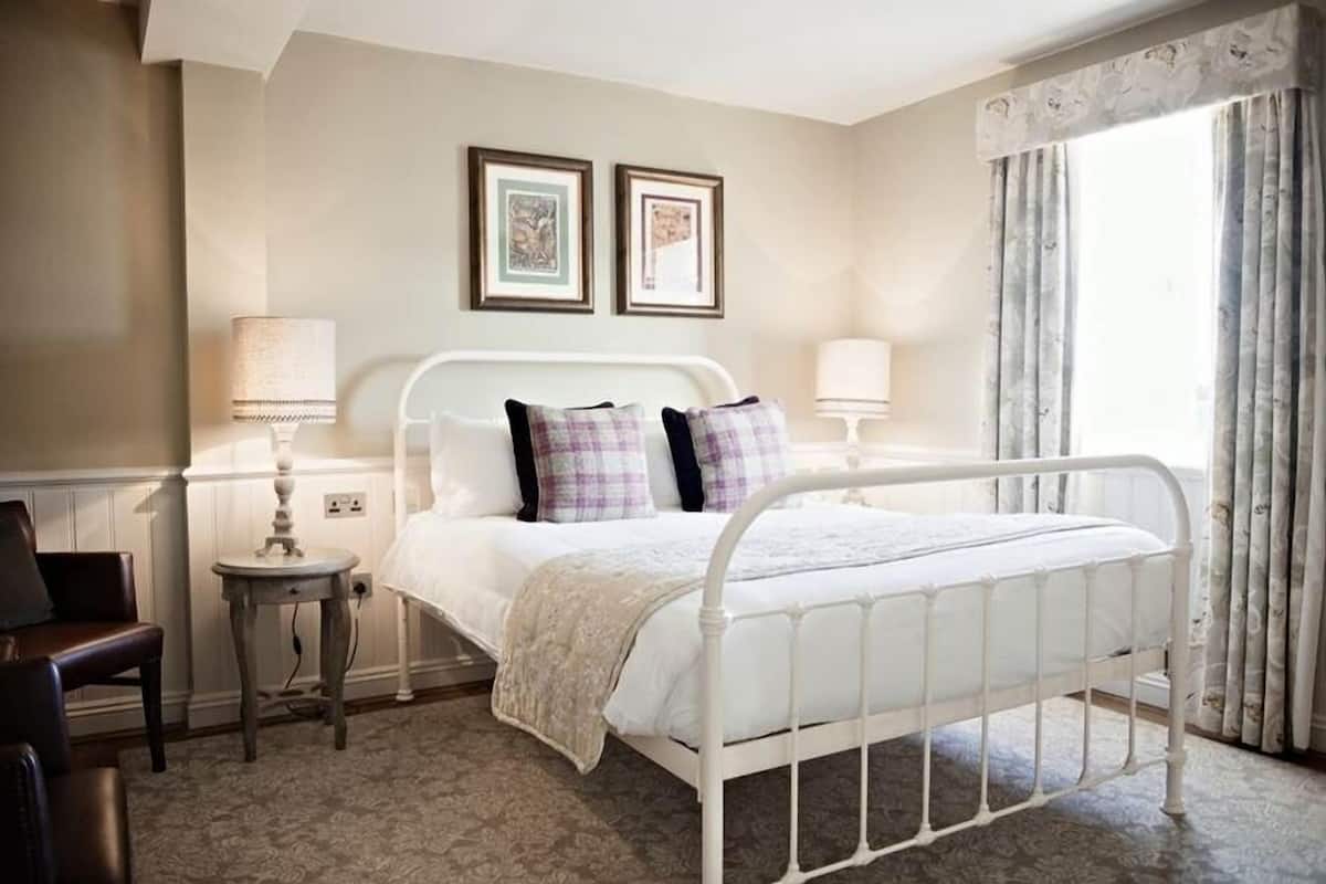 Une chambre à coucher bien rangée, avec un lit en métal blanc, une petite table de chevet avec une lampe et deux tableaux encadrés accrochés au mur.