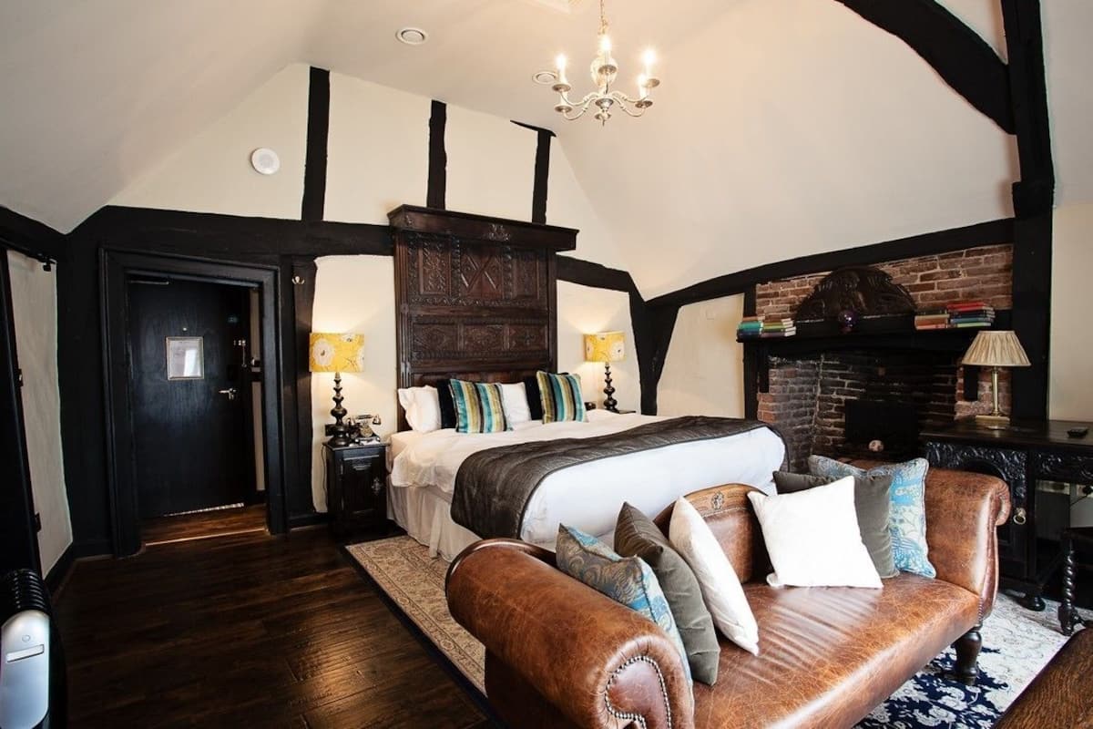 Une chambre à coucher avec un grand lit, un canapé en cuir, une cheminée et un lustre.