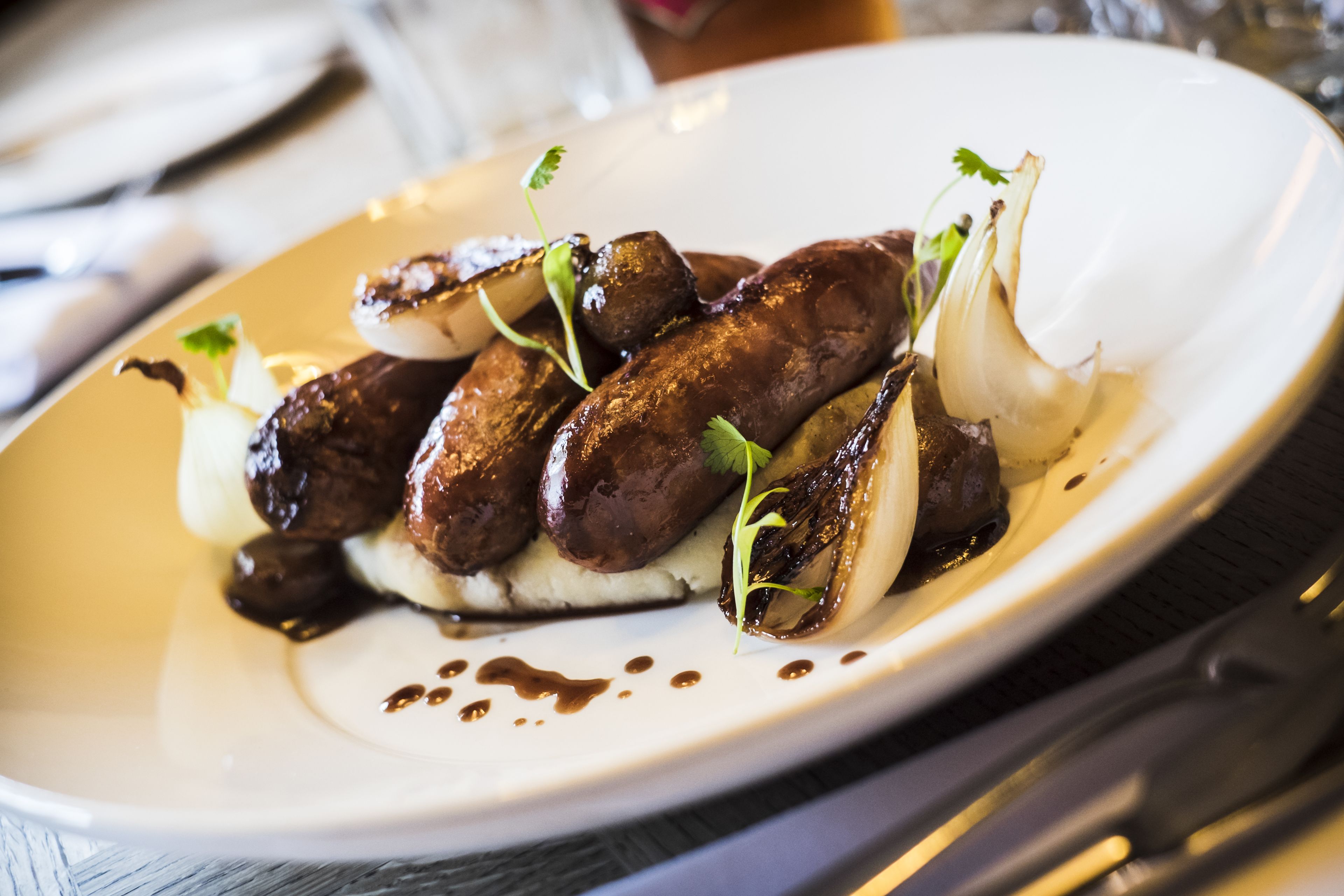 A white plate with grilled sausages, onions, and a garnish on a wooden table.