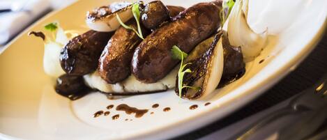 A white plate with grilled sausages, onions, and a garnish on a wooden table.