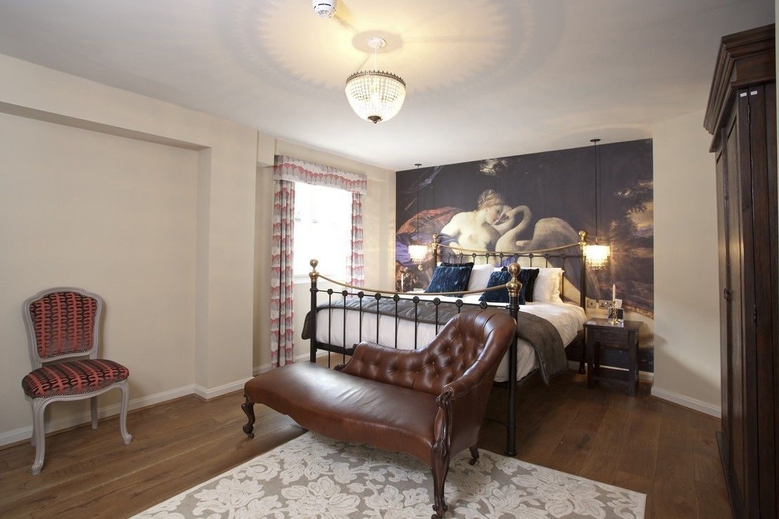 Een slaapkamer met een bed, een chaise longue, een fauteuil, een kroonluchter en een groot schilderij aan de muur.