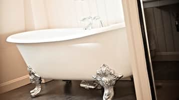 A white clawfoot bathtub with ornate metal feet in a bathroom with a dark floor and light walls.