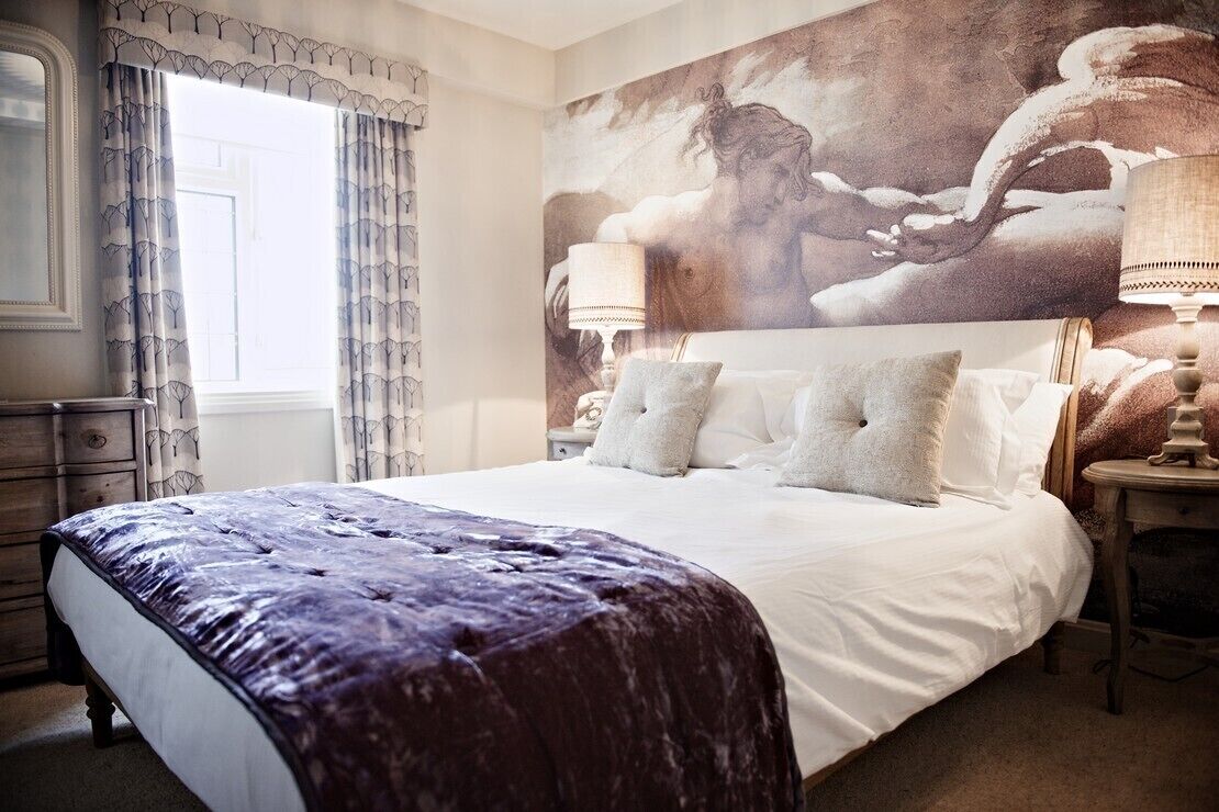 Een slaapkamer met een groot bed, twee nachtkastjes en een muurschildering.