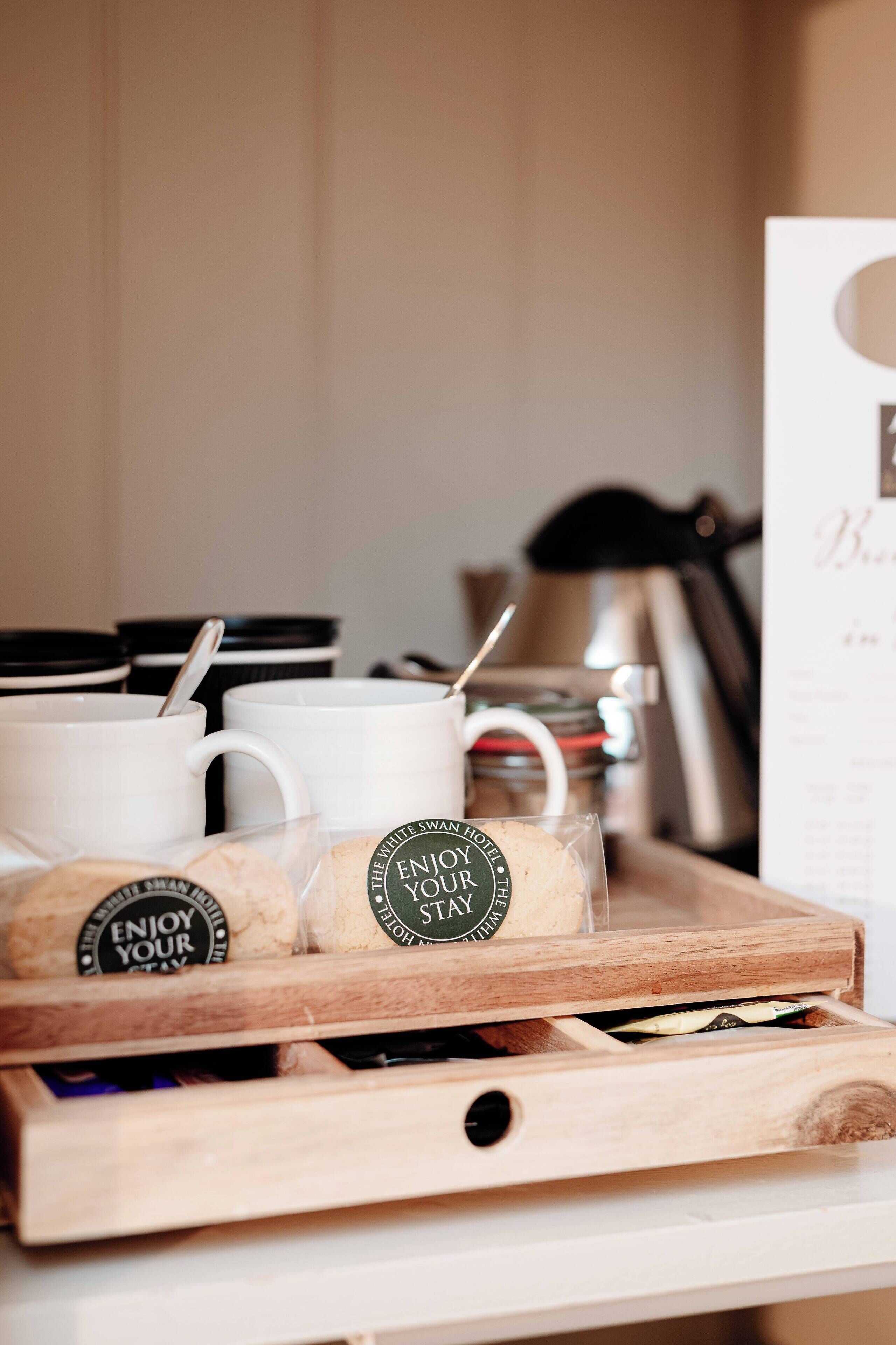 Een dienblad met witte mokken en koekjes, elk met een 'Enjoy Your Stay' label.
