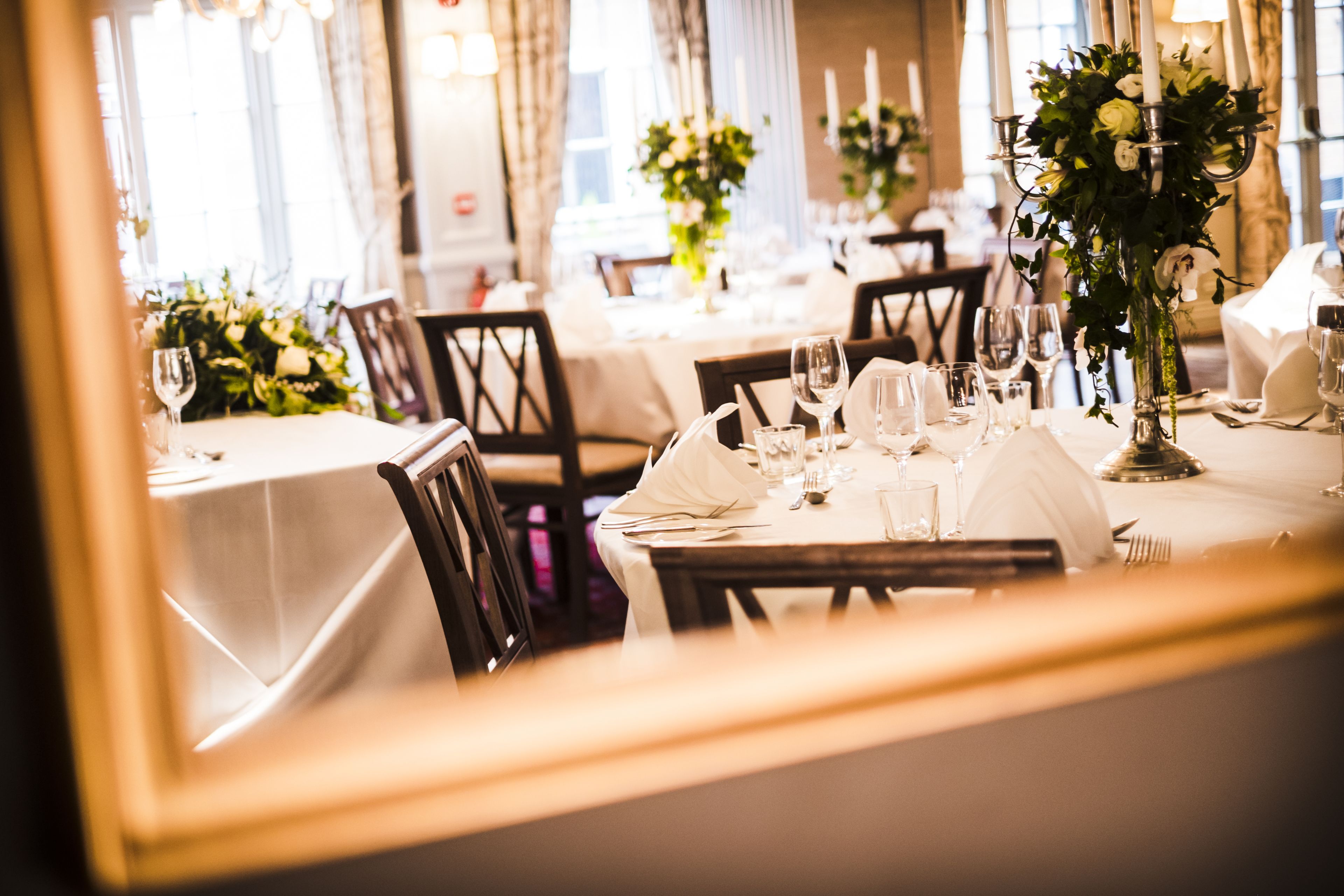 A dining area with tables set for a meal, featuring white tablecloths, glassware, and floral centerpieces.