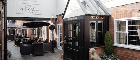 Zona de recepción del Hotel White Swan, con una puerta negra, una estatua de perro y asientos exteriores con sombrillas.