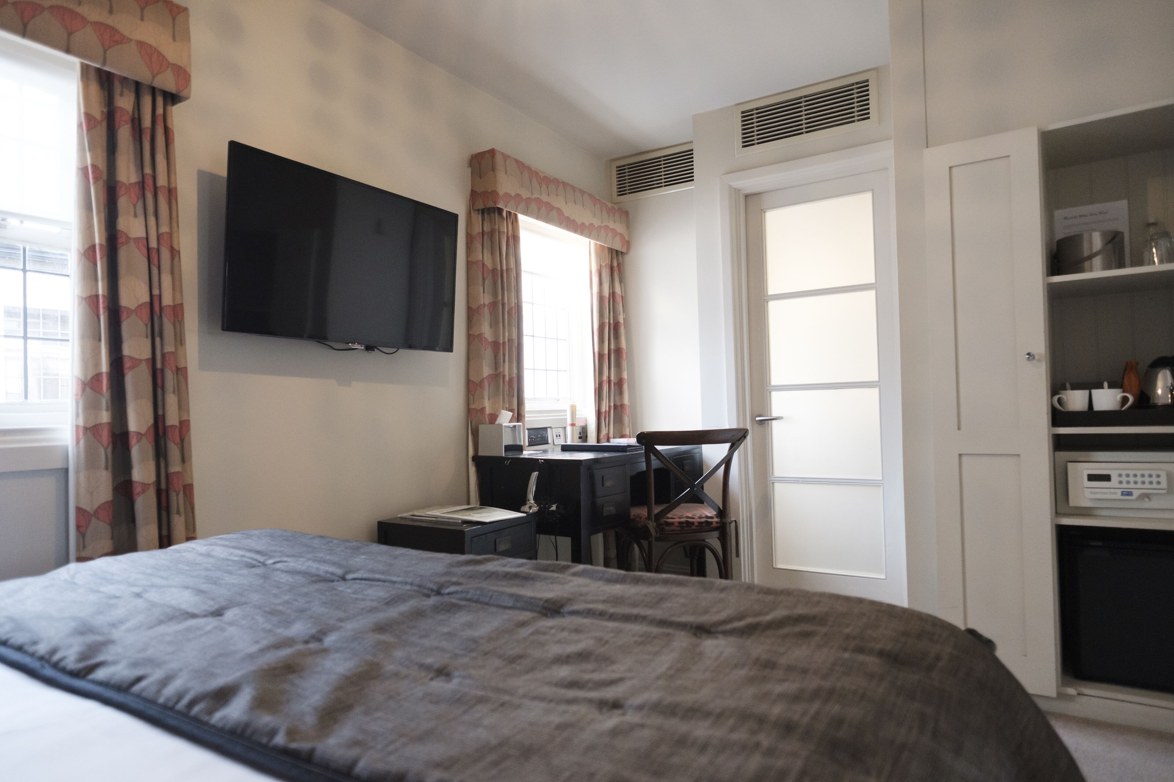 A hotel room with a bed, a desk with a chair, a television, and a kitchenette.