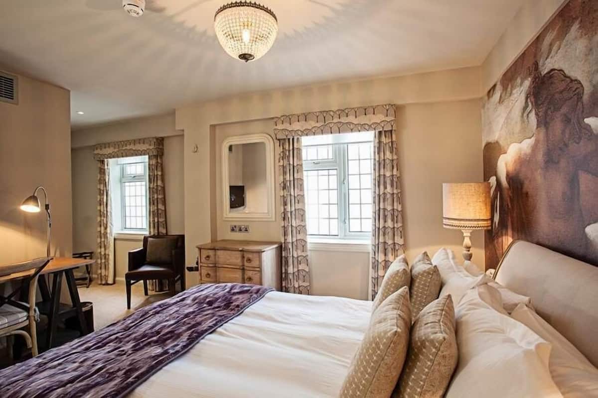 Une chambre d’hôtel avec un grand lit, un bureau, une chaise, une commode et un tableau au mur.