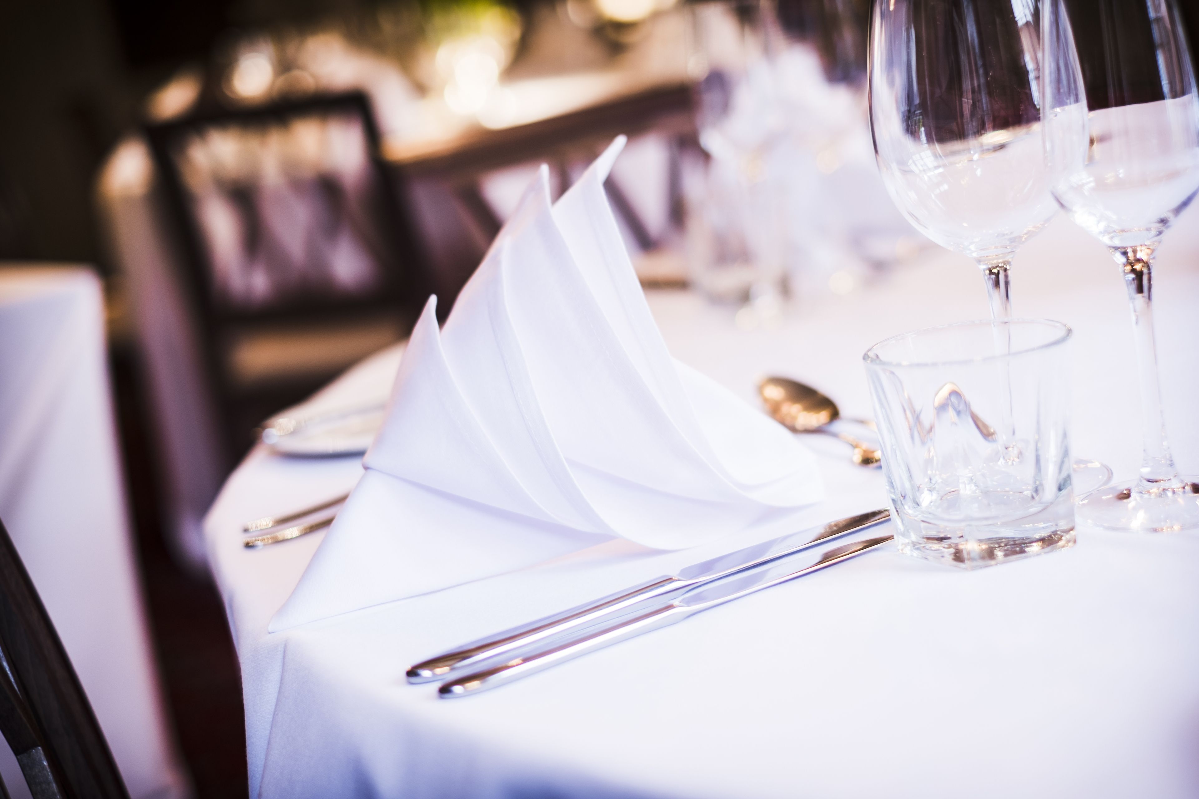 A table set with white tablecloth, silverware, and clear glassware.
