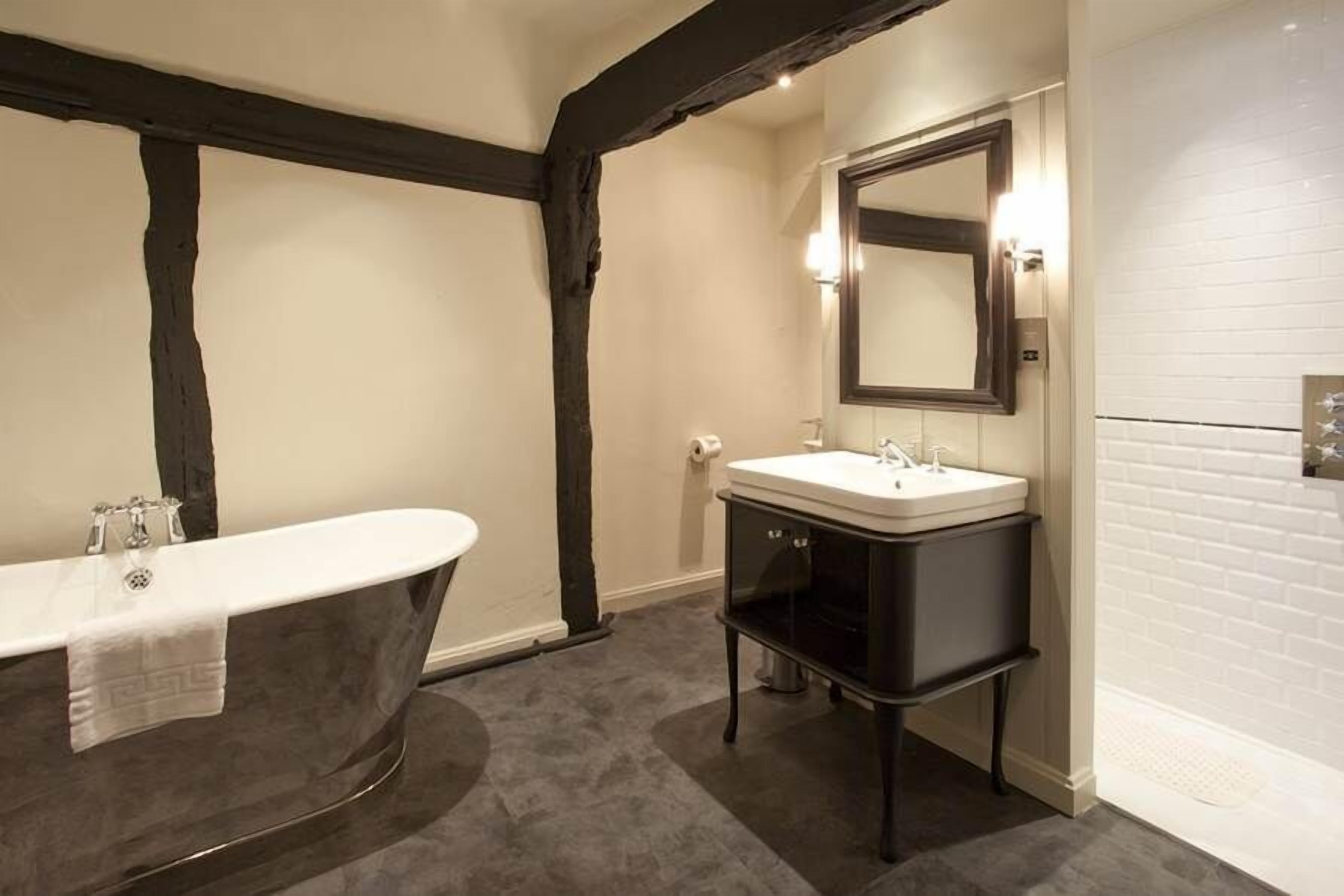 A bathroom with a freestanding bathtub, a vanity with a mirror, and a white tiled wall.