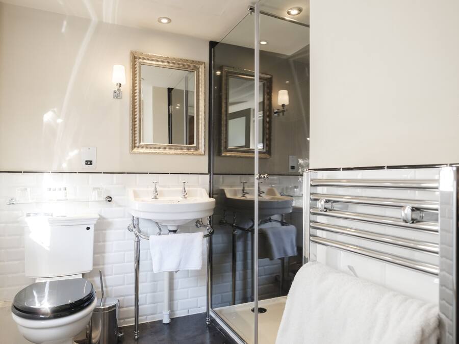 Une salle de bain moderne comprenant des toilettes, deux lavabos, une douche à l’italienne avec des parois en verre et un grand miroir.