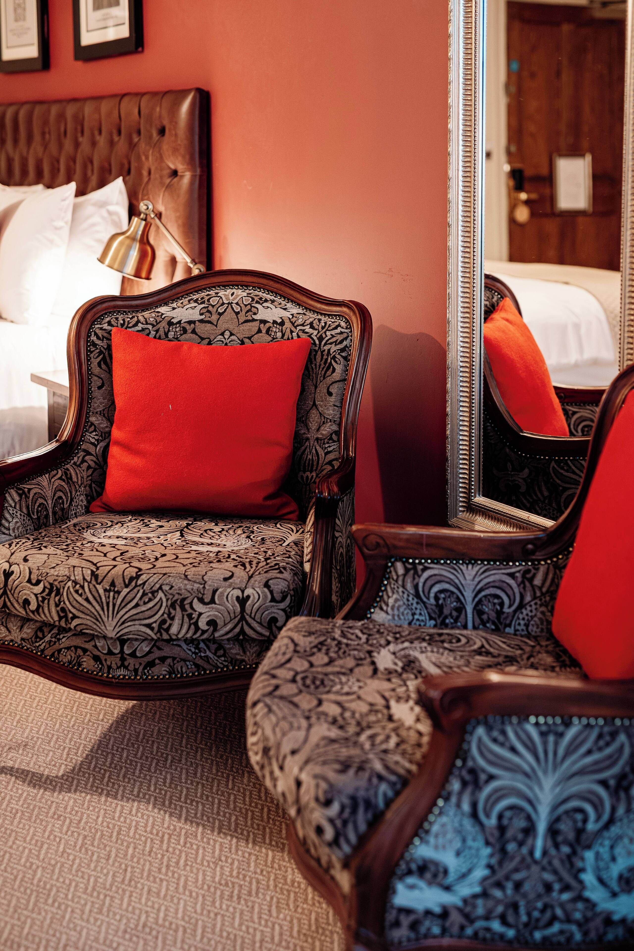 A room with a large bed, a wooden headboard, a red pillow, and a mirror reflecting part of the room.