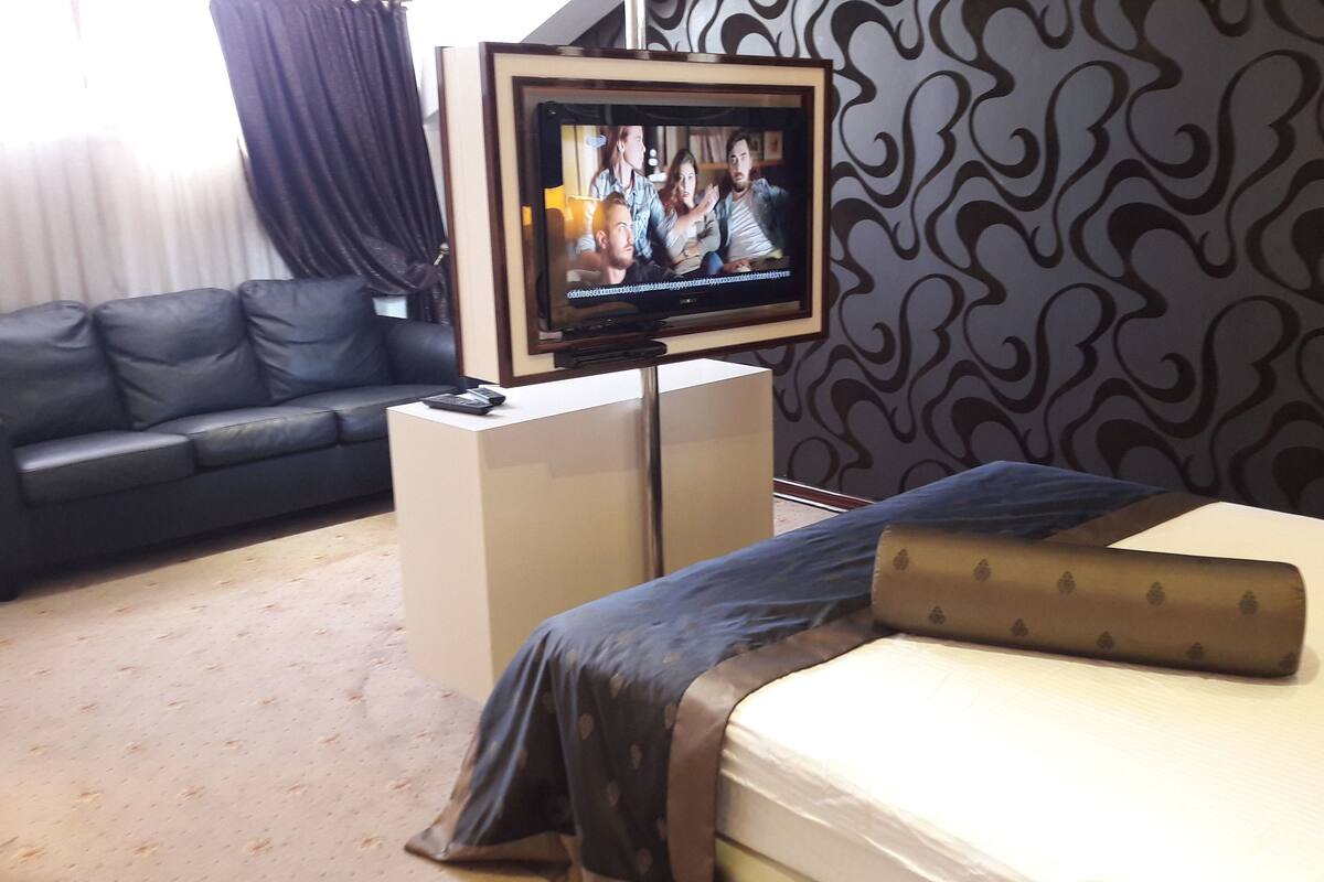 Una habitación de hotel con cama, sofá, televisor sobre un mueble bajo y pared con estampado.