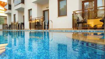 Una piscina interior moderna con agua azul cristalina, rodeada por un edificio blanco con balcones y ventanales amplios.