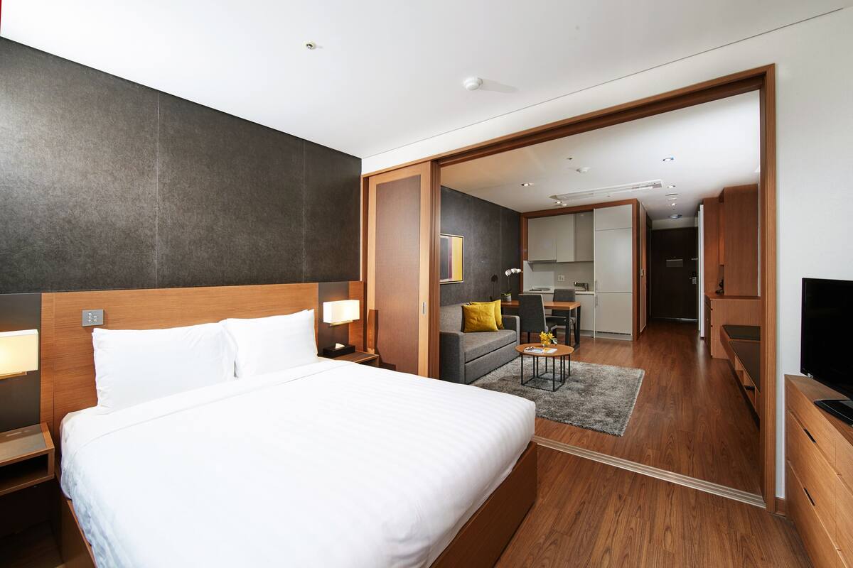 Habitación de hotel con una cama grande, un escritorio con silla, un sofá y un televisor.
