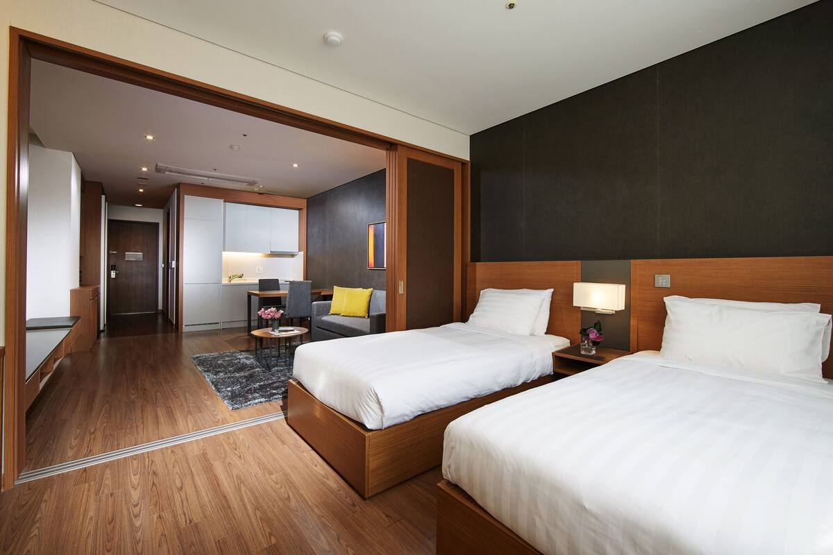 Habitación de hotel con dos camas, un escritorio, una silla, una mesita con un jarrón y un sofá.