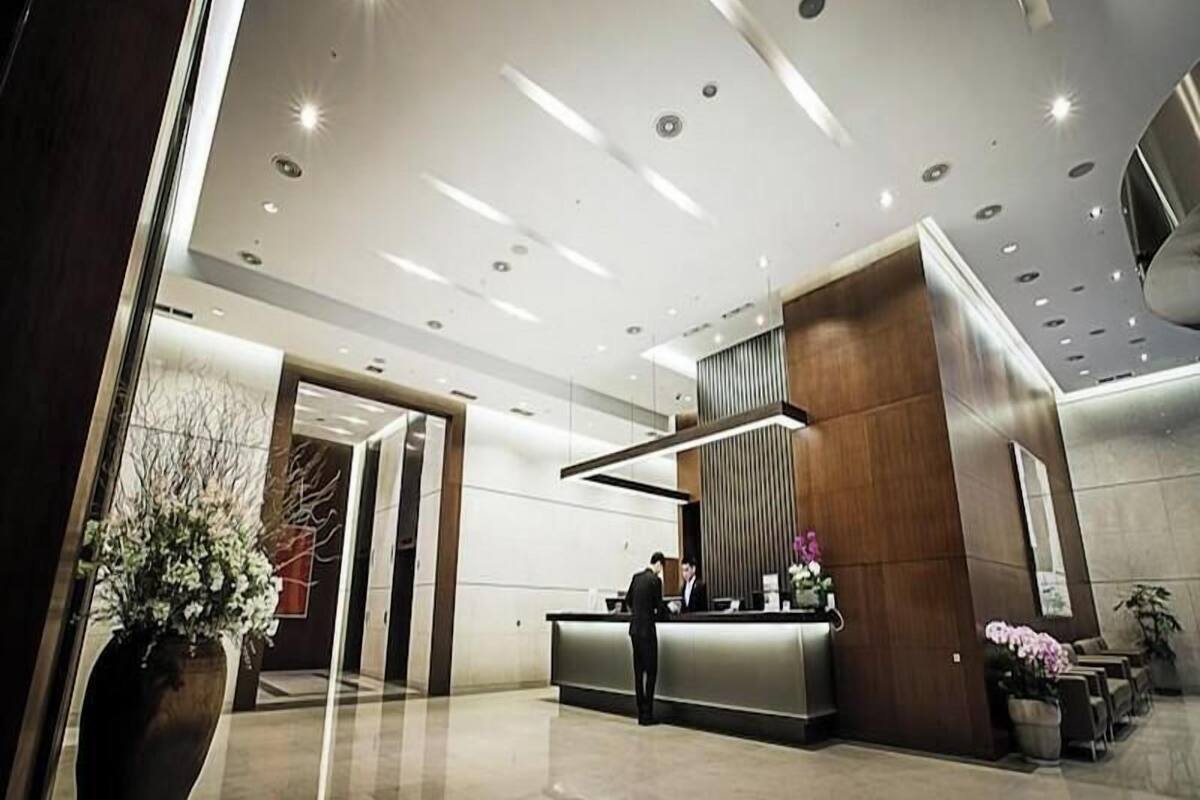 Un moderno vestíbulo de hotel con una mesa de recepción, un jarrón grande con flores y un área de descanso con mesas y sillas.