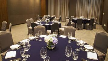 Un salón de conferencias con mesas redondas, cada una con cubiertos, platos y vasos.