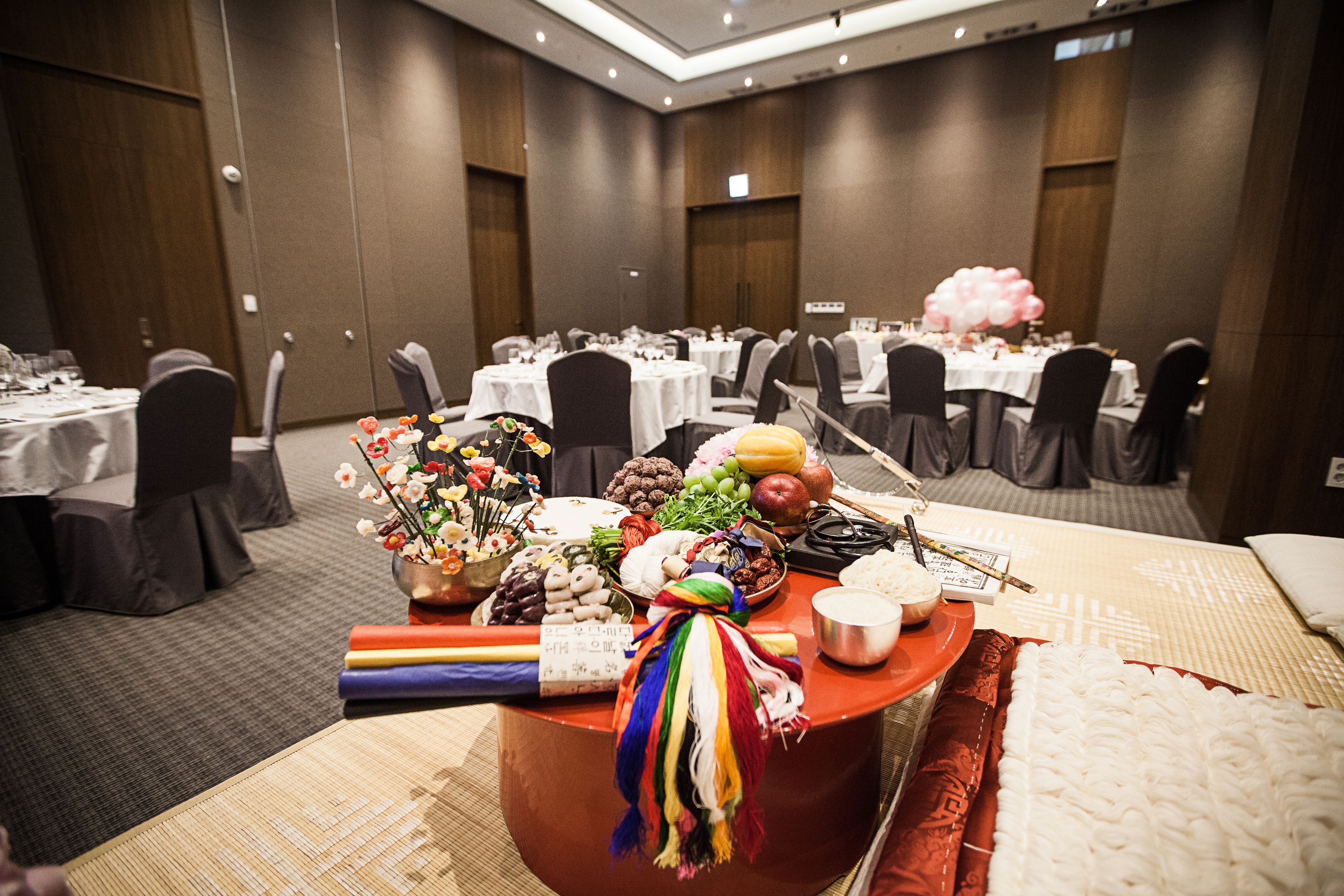 A banquet hall with round tables, chairs, and a buffet table with various food items and decorations.