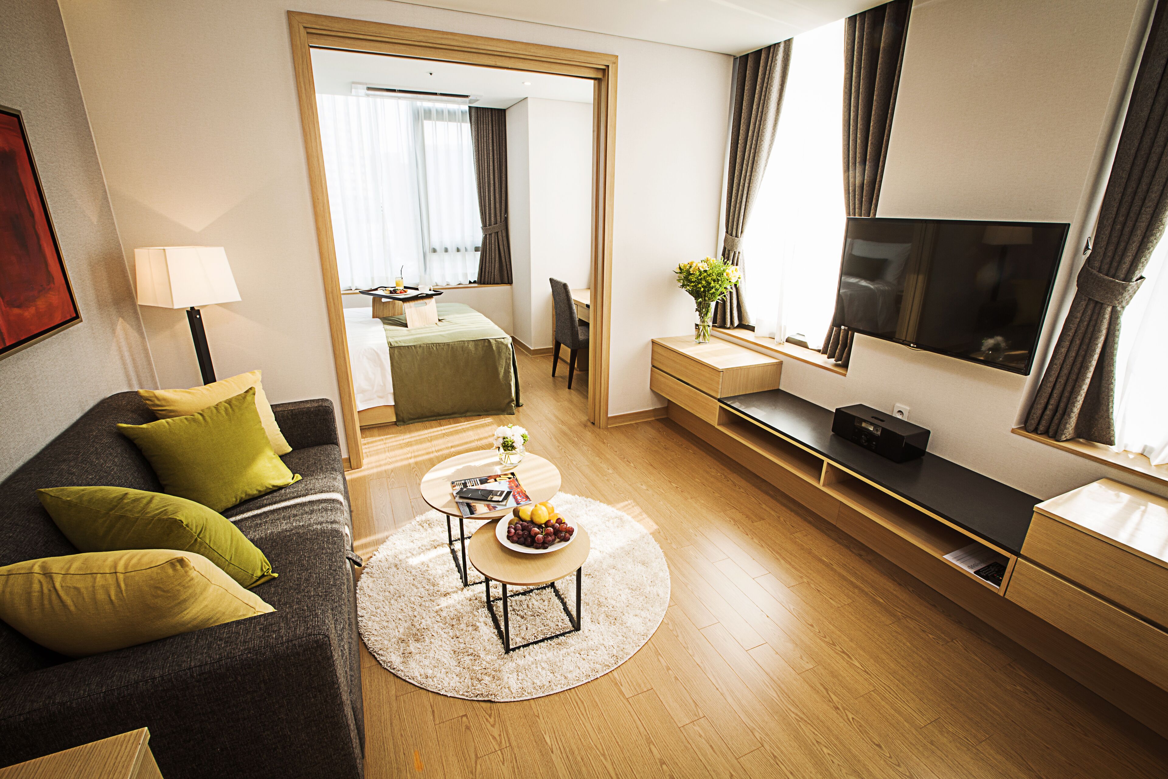 Habitación de hotel moderna con sofá, mesa de centro, televisor, escritorio y espejo.