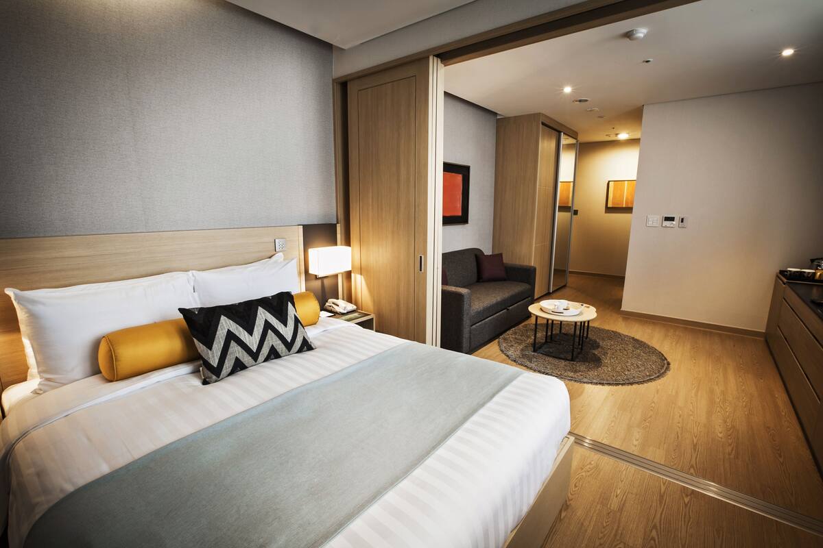 Una habitación de hotel moderna con una cama grande, un escritorio con lámpara, un sofá y una pequeña mesa.