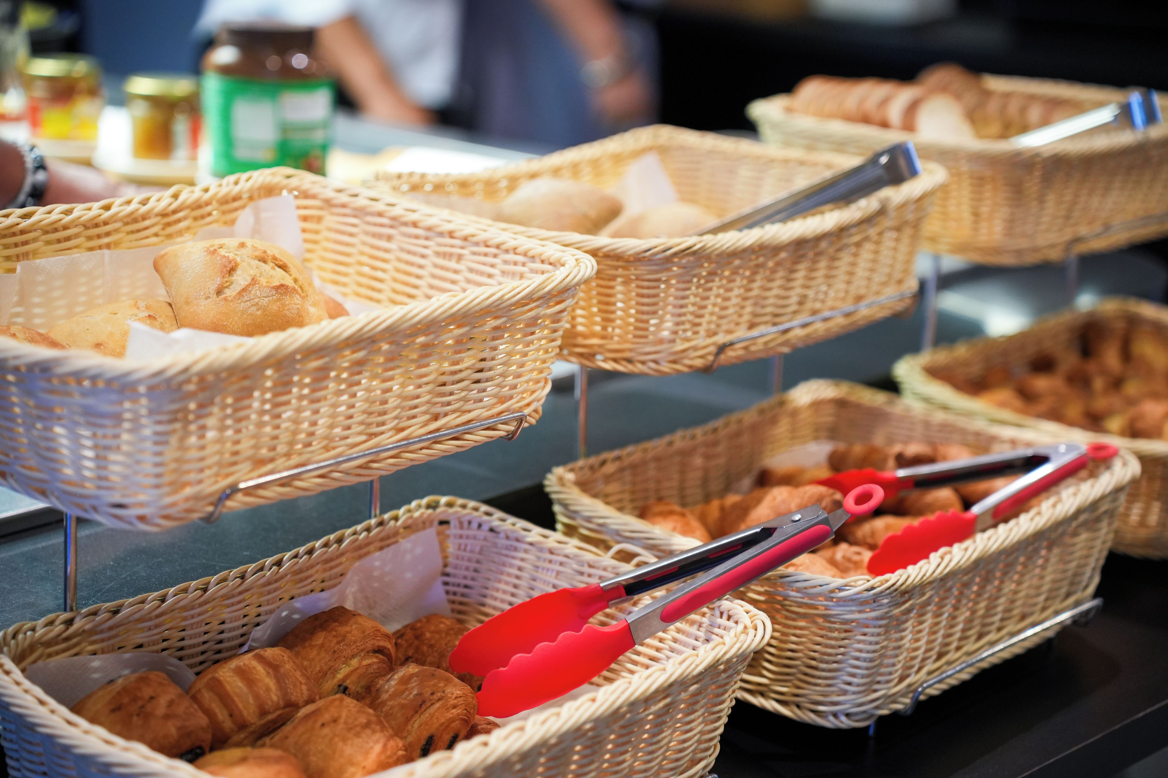 Wicker baskets filled with bread and pastries, with red tongs placed on top.