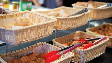 Wicker baskets filled with bread and pastries, with red tongs placed on top.